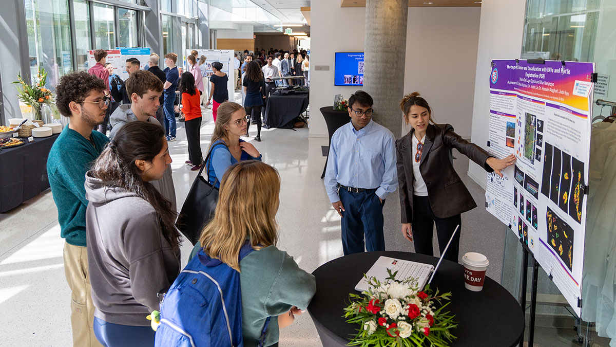 Wide shot of student explaining poster in the foreground and attendees in the background
